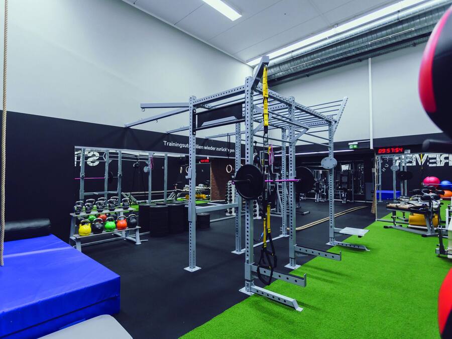 A gym with weightlifting equipment, a blue mat, and a green turf area.