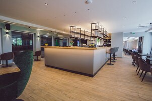 Zona de bar moderna con una isla central, taburetes y un área de estar con mesas y sillas.