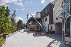 Un edificio moderno con una escalera que lleva a un área cubierta, un coche estacionado al frente y un cielo despejado.