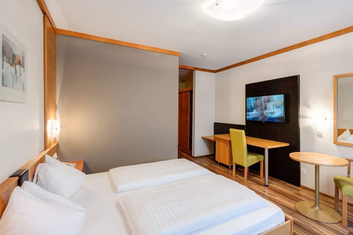 Habitación de hotel con dos camas, un escritorio, una silla, un televisor y una mesita.
