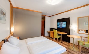 A hotel room with two beds, a desk, a chair, a TV, and a small table.