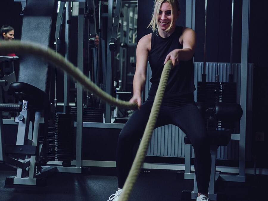 A person using a battle rope in a gym with various exercise equipment.