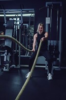Una persona usando una cuerda de batalla en un gimnasio con varios equipos de ejercicio.