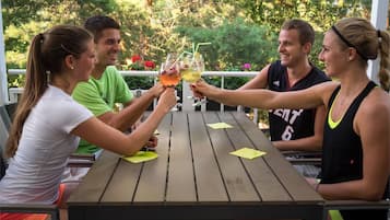 Un grupo de personas brindando con bebidas en una mesa de madera al aire libre, con vistas a árboles y flores.