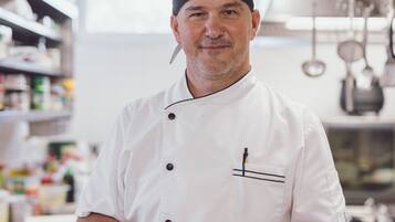 A chef in a white uniform holding a plate of food in a kitchen.