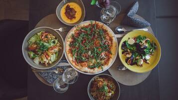 Una mesa servida con diversos platos, incluyendo pizza, ensalada y sopa, junto con copas de vino y cubiertos.
