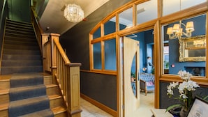 A staircase with wooden railings and carpeted steps leading to a room with a curved wooden door, a mirror, and a chandelier. - Jolyon's Boutique Hotel (Cardiff)