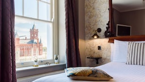 A hotel room with a large window, a bed with striped pillows, a wooden headboard, a nightstand with a lamp, and a wall with a map design. - Jolyon's Boutique Hotel (Cardiff)