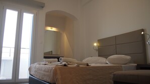A hotel room with a bed, a nightstand, a mirror, and a sliding door leading to a balcony. - Homer's Inn Hotel (Ios)