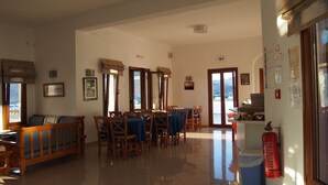 A spacious dining area with wooden furniture and a view of the mountains through the open door. - Homer's Inn Hotel (Ios)