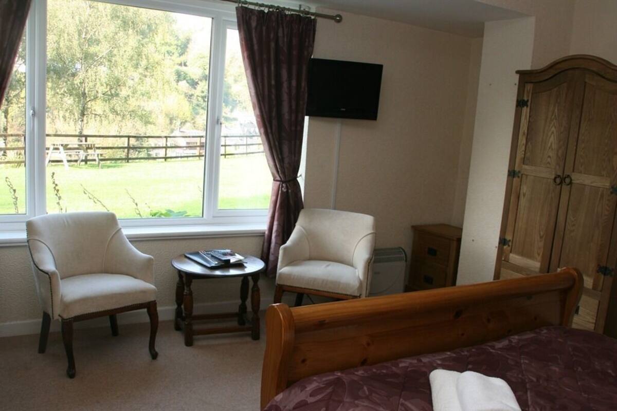 A bedroom with a bed, two armchairs, a small table, a TV, and a wardrobe.