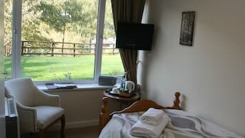 Ein Hotelzimmer mit einem Bett, einem Sessel, einem Fernseher und einem Fenster mit Blick auf eine Wiese.