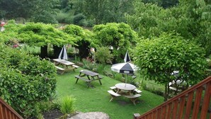 A garden patio with picnic tables and umbrellas, surrounded by lush greenery. - The Royal Lodge (Ross-on-Wye)