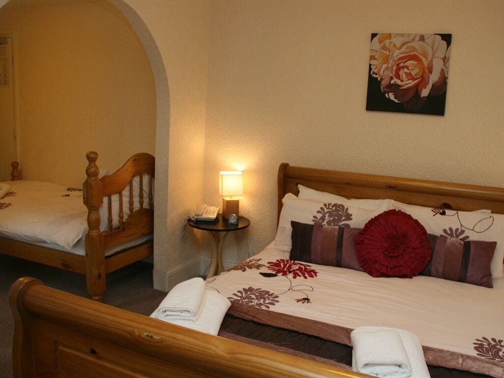 Una habitación de hotel con dos camas de madera, una mesita de noche con lámpara y una obra de arte floral en la pared.