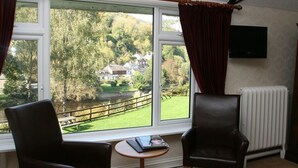 A room with two leather chairs, a small table, a window with curtains, and a radiator. - The Royal Lodge (Ross-on-Wye)