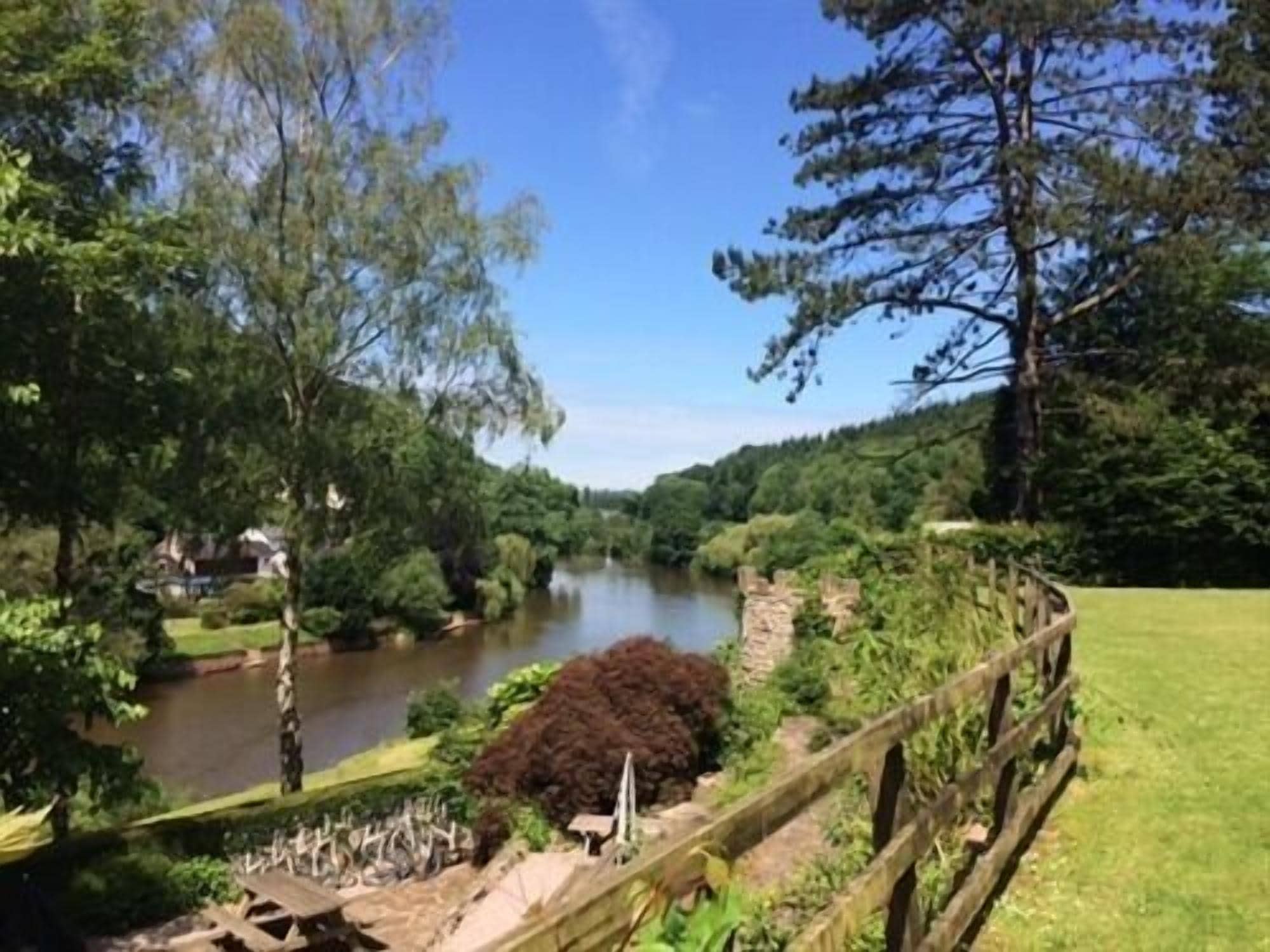 Une vue sur la rivière, avec une clôture en bois, de la verdure et un ciel dégagé.
