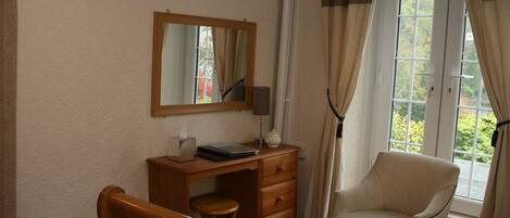 A bedroom with a wooden bed, a desk with a chair, a mirror, and a window with curtains.