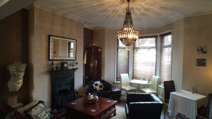 A traditional living room with a fireplace, a chandelier, and a dining area with a table and chairs. - Tyrosa Rooms   (Cardiff)