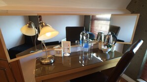 A hotel room desk with a lamp, two water bottles, a coffee maker, and a small bowl. - Tyrosa Rooms   (Cardiff)