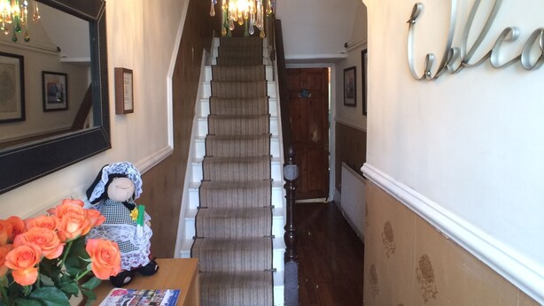 A grand staircase with a chandelier, a welcome sign, a mirror, and a small table with roses and a price tag. - Tyrosa Rooms   (Cardiff)