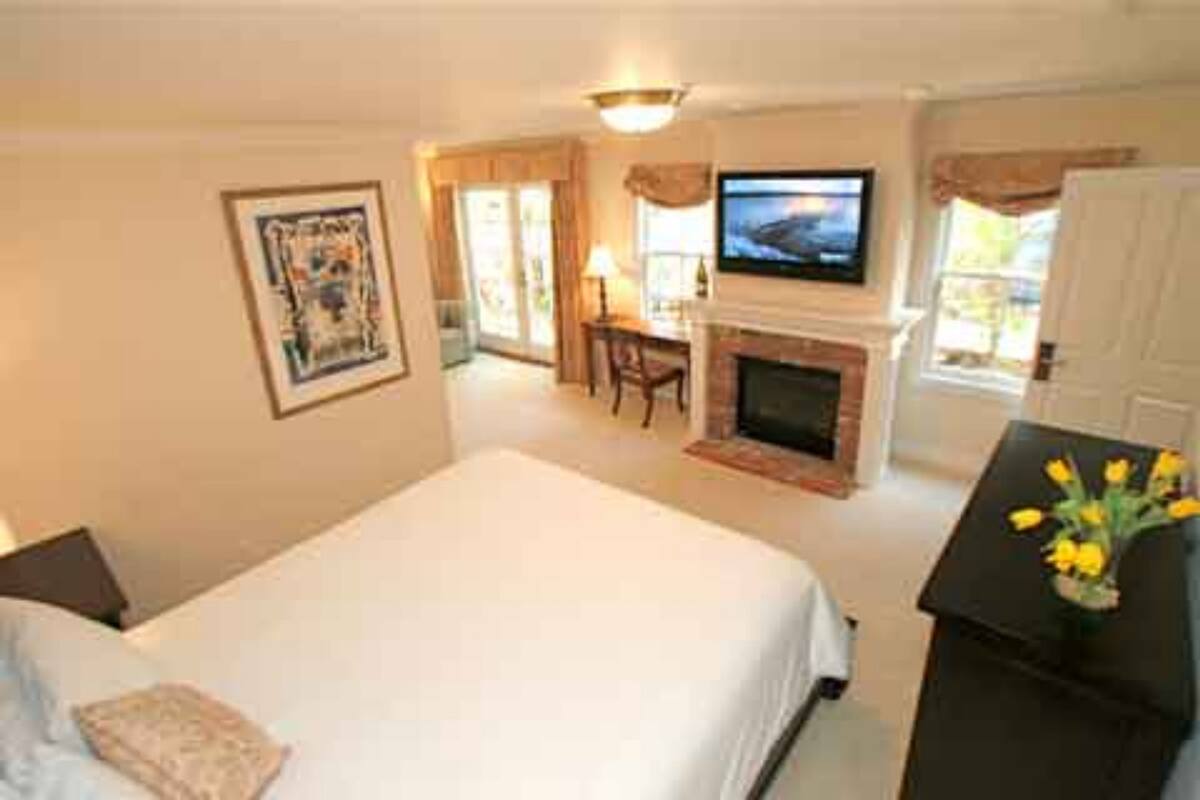 A bedroom with a bed, a television, a fireplace, and a desk with a lamp.