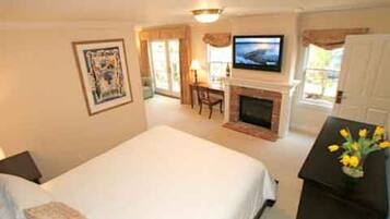 A bedroom with a bed, a television, a fireplace, and a desk with a lamp.