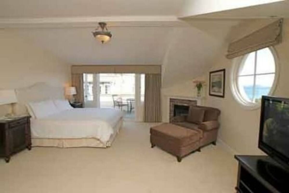 A spacious bedroom with a large bed, a television, a fireplace, and a view of the outdoors.
