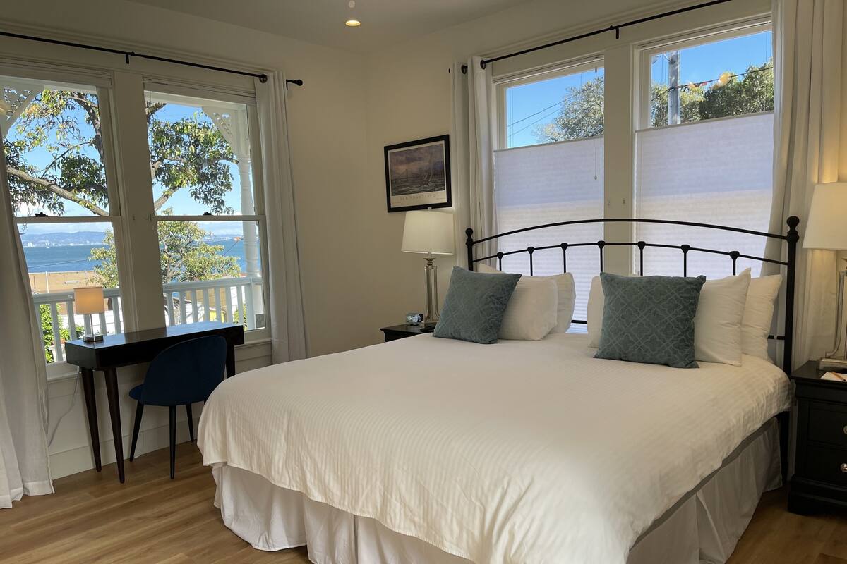 A bedroom with a bed, a desk, and a view of the sea.
