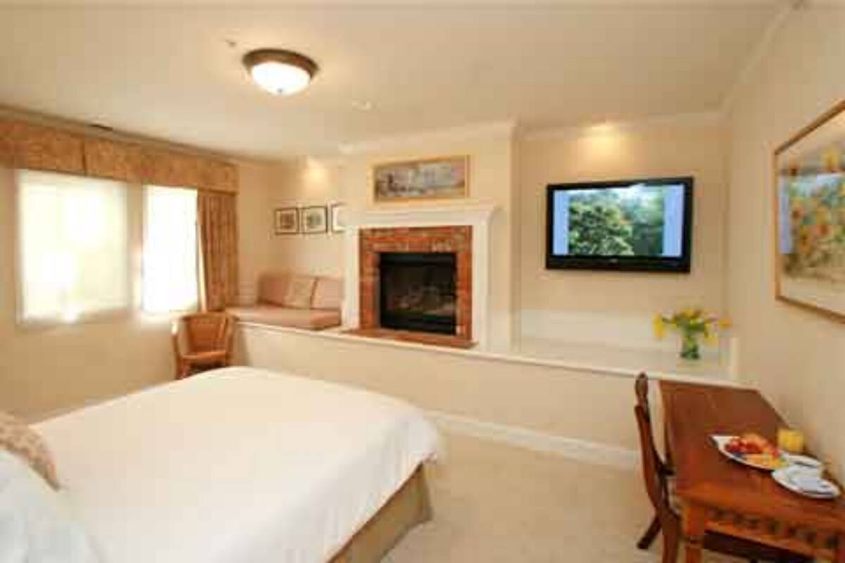 A hotel room with a bed, a seating area with a table, a fireplace, and a television on the wall.