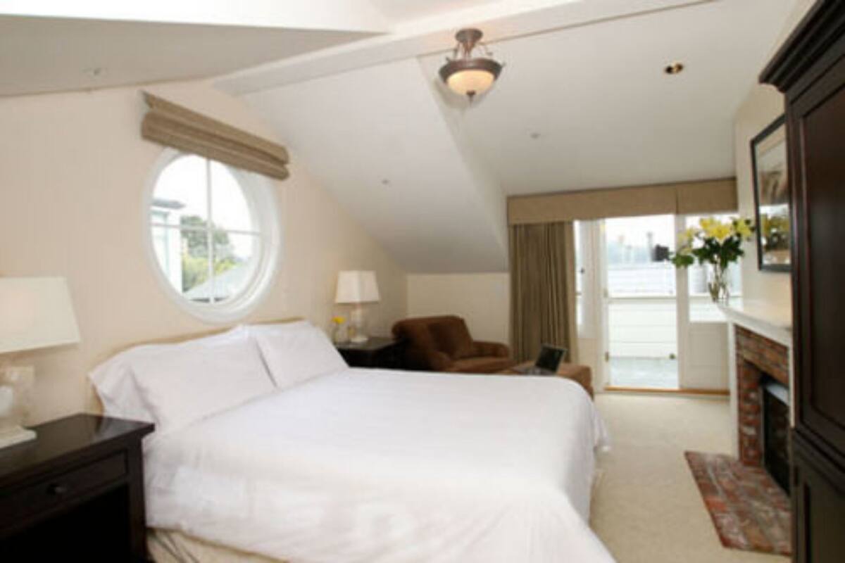 A hotel room with a large bed, a round window, a chair, a lamp, and a fireplace.