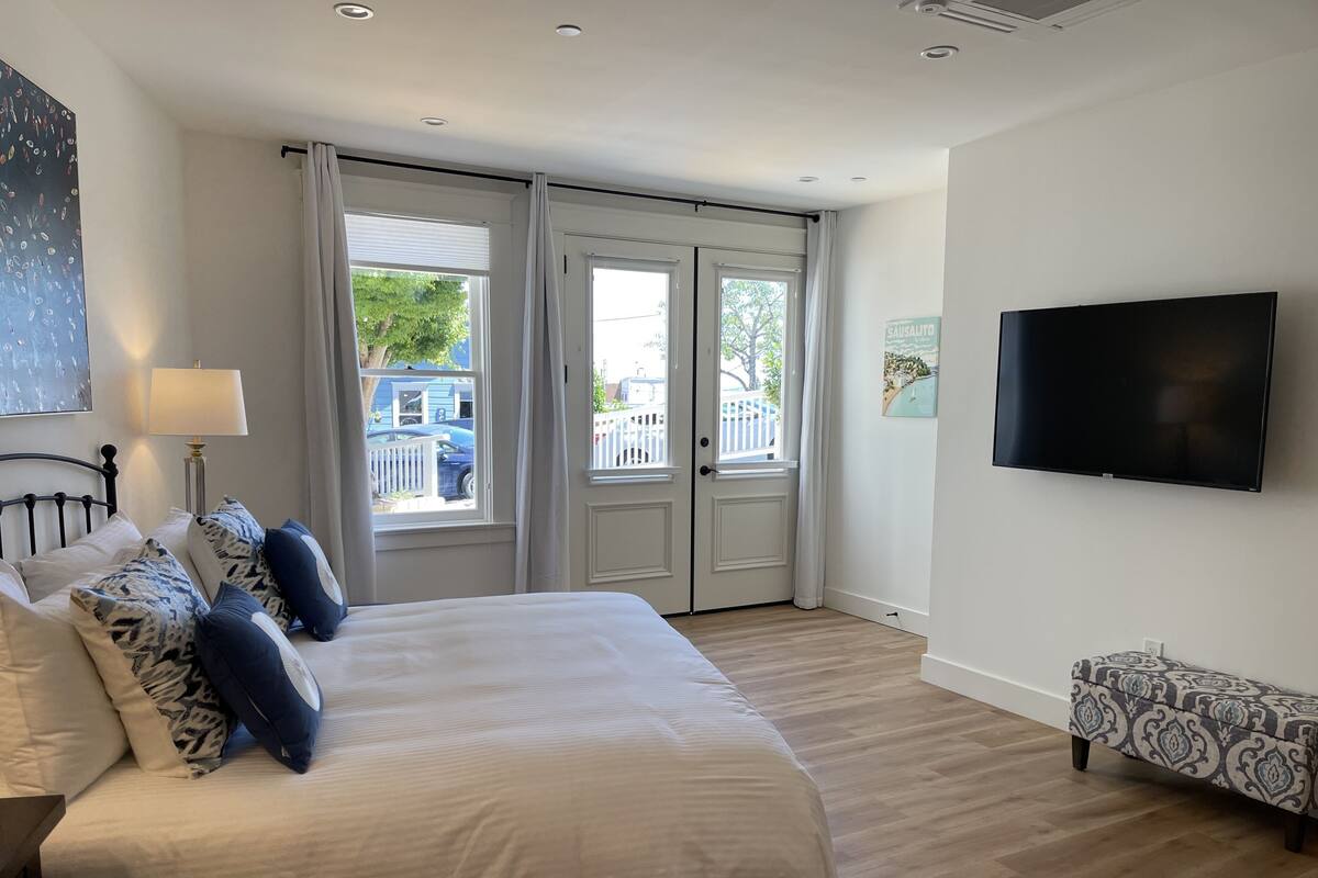 A bedroom with a bed, a TV, a bench, and a window with curtains.