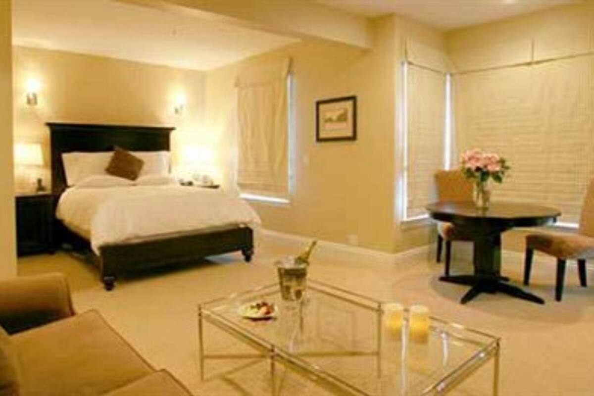 A hotel room with a bed, a glass coffee table, a chair, and a small table with a vase of flowers.