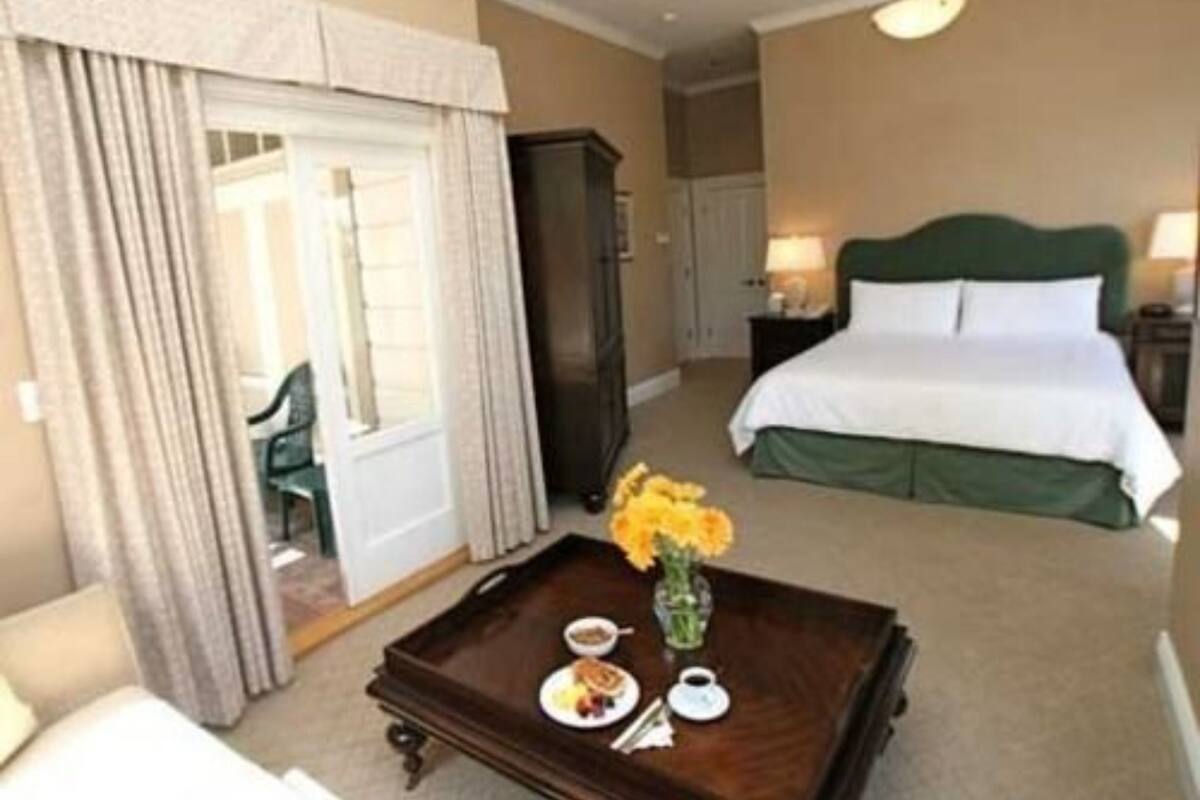 A hotel room with a bed, a bedside table with a vase of flowers, a tray with breakfast items, and a view of the hallway.