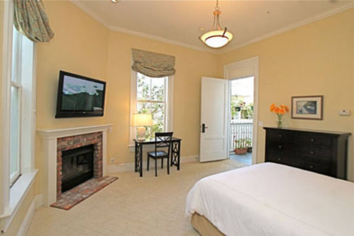 A bedroom with a fireplace, a television, a bed, a dresser, and a door leading to a balcony.