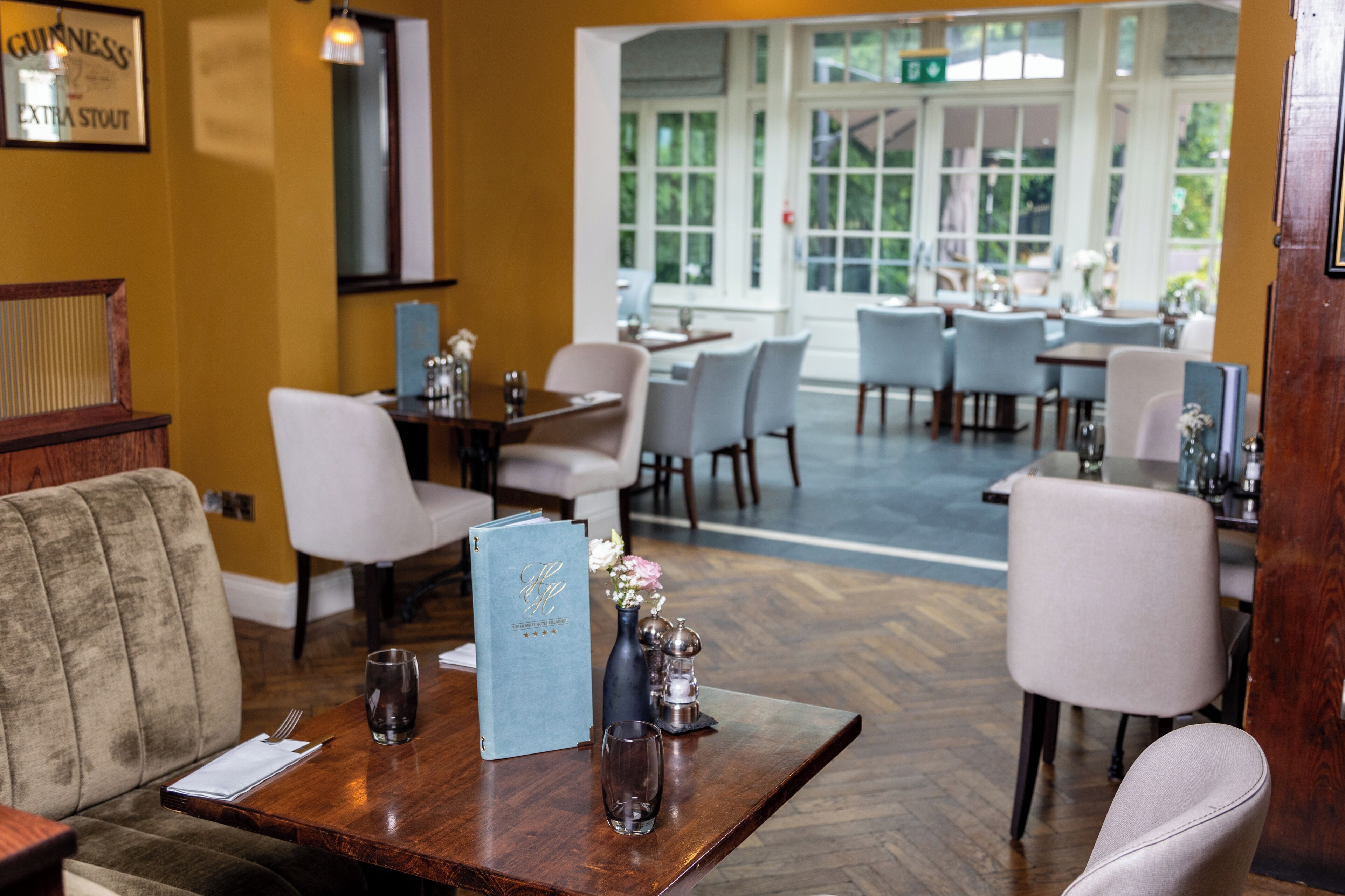 A restaurant interior with a wooden table set for dining, a menu, and a vase with flowers.