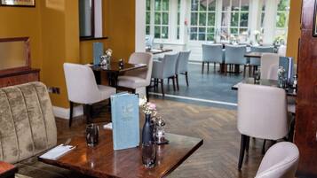 L'intérieur d'un restaurant, avec une table en bois dressée pour le repas, un menu et un vase rempli de fleurs.