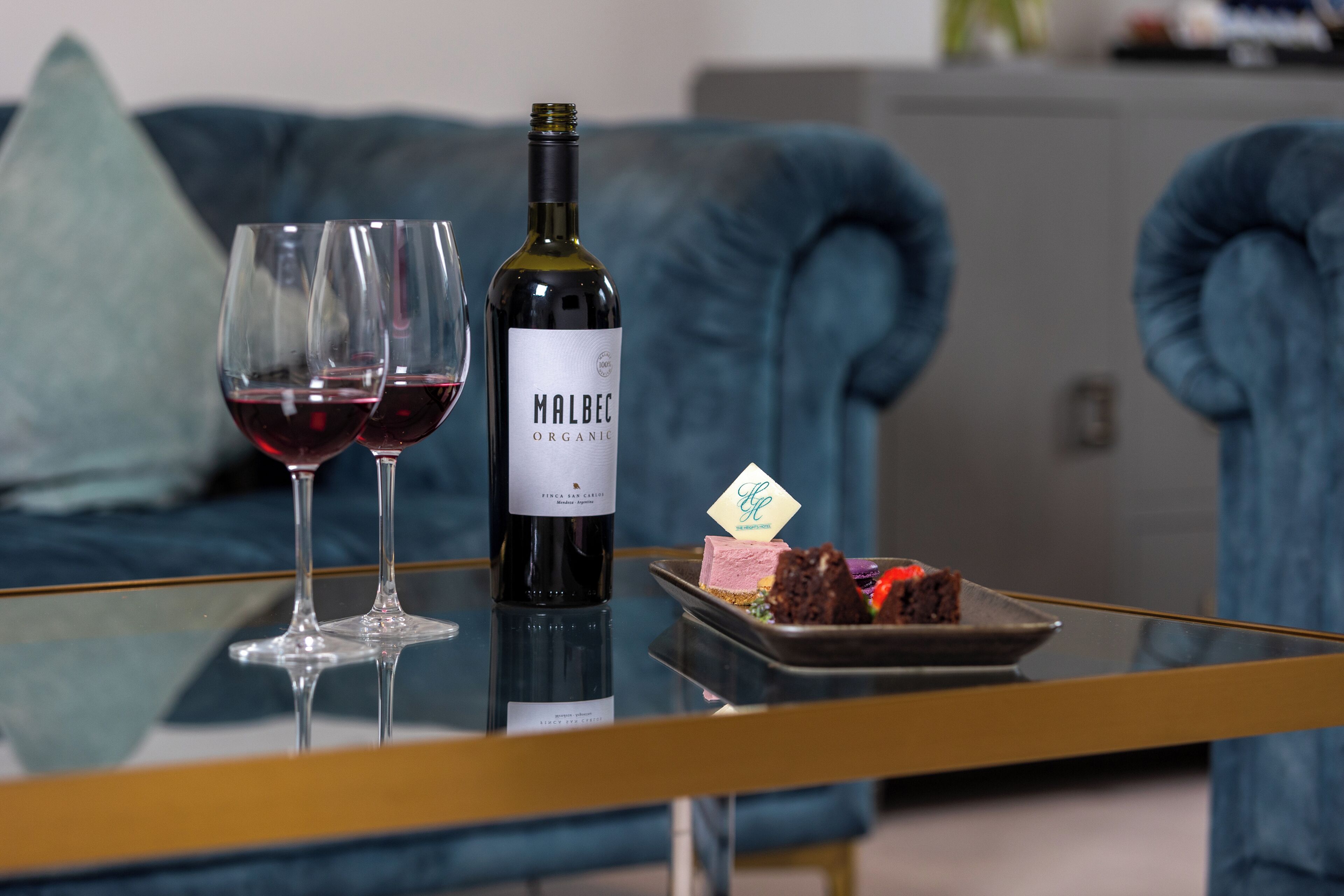 Eine Flasche Malbec, zwei Weingläser und ein Dessert auf einem Glastisch.