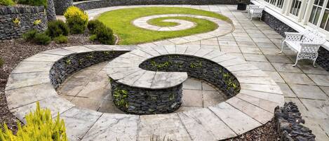 Une terrasse aménagée avec un motif en spirale, des sièges en pierre et une clôture blanche.
