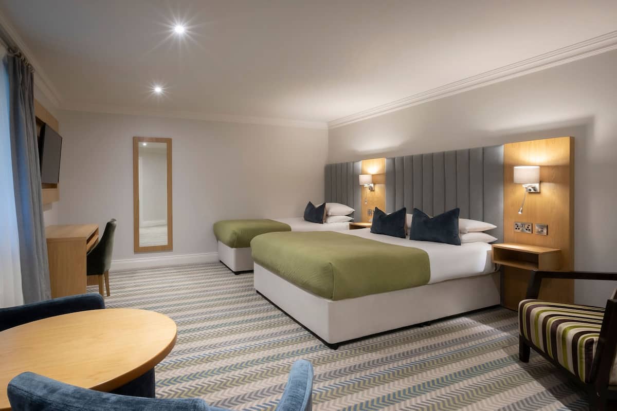 A hotel room with two beds, a desk, a chair, a round table, and a patterned carpet.