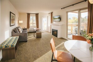 A hotel room with a sofa, a small table, a fireplace, a TV, and a balcony with a view.