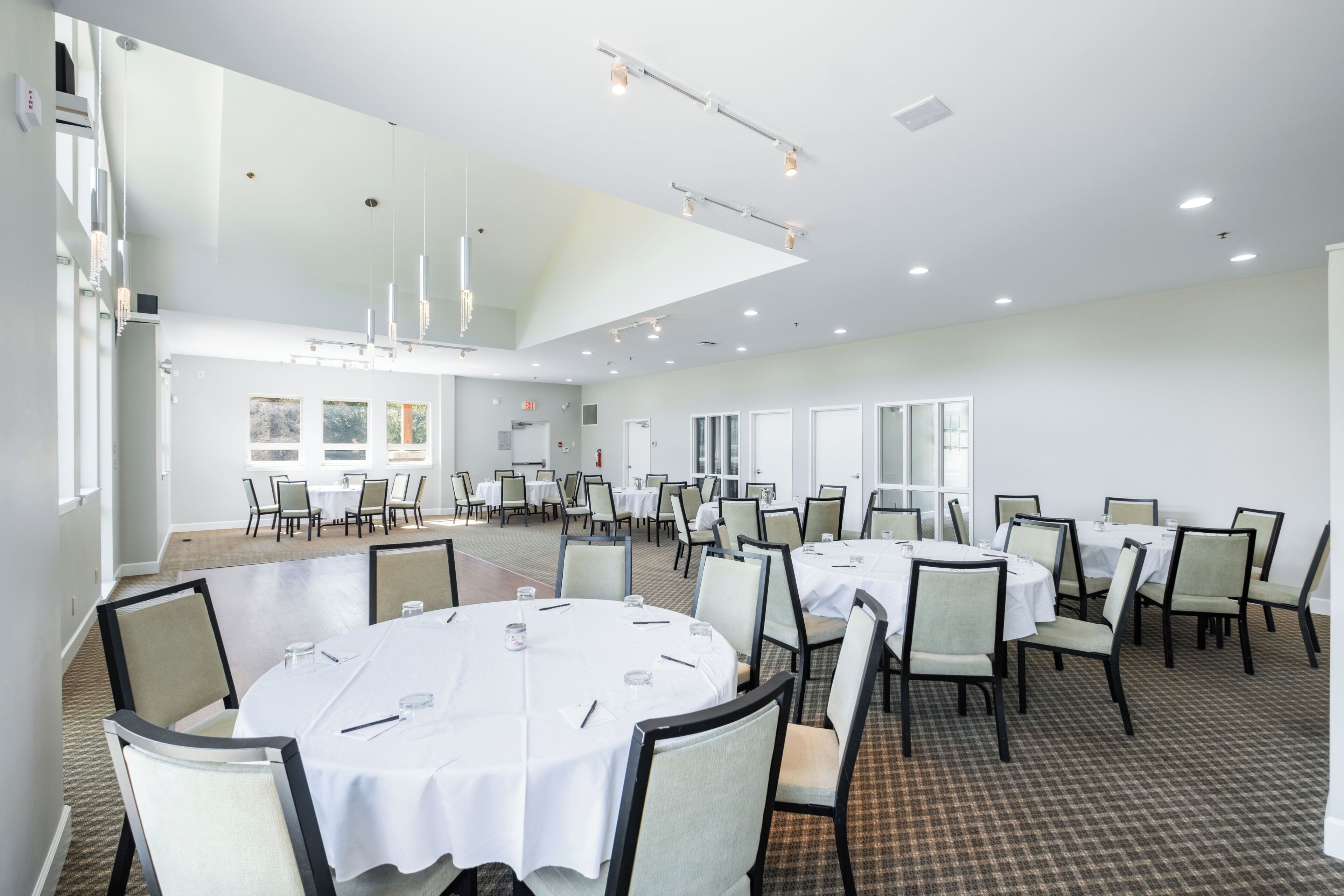 A spacious conference room with round tables, chairs, and a high ceiling with recessed lighting.