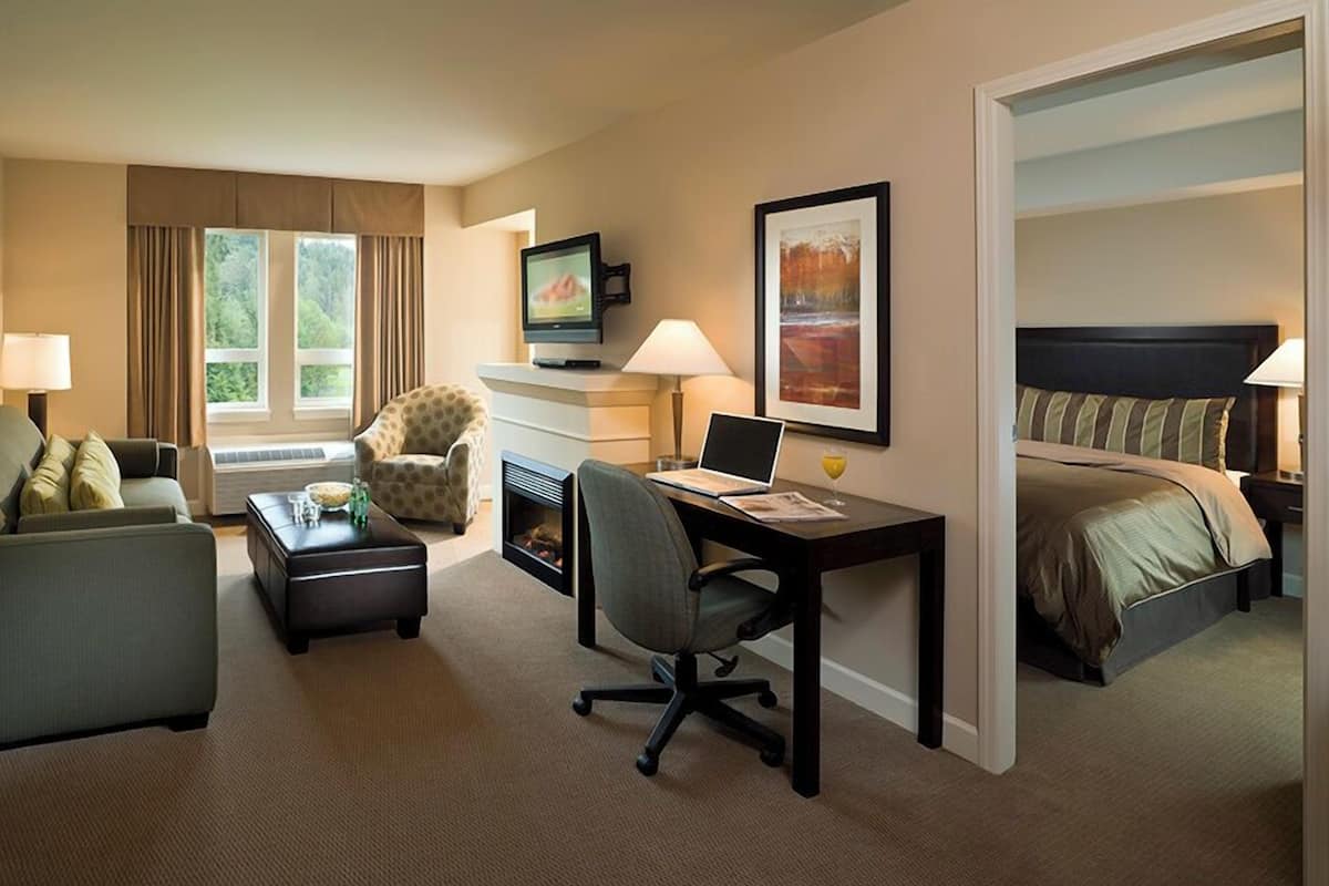Una habitación de hotel con sofá, escritorio con computadora, televisión, chimenea y cama.