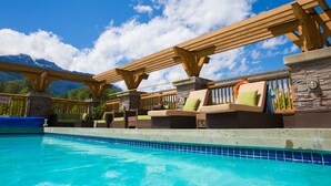 A poolside area with wooden pergolas, lounge chairs, and a view of mountains. - Executive Suites Hotel & Resort, Squamish (Squamish)