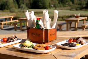 A picnic table with various dishes, including a sandwich, salad, and meat, along with napkins and condiments in a wooden box labeled "JP WISER'S".