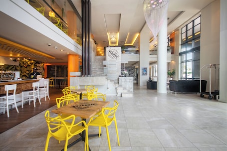 A spacious lobby with a central staircase, yellow chairs, and a wooden table.