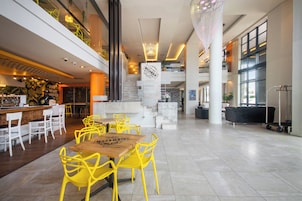 A spacious lobby with a central staircase, yellow chairs, and a wooden table.