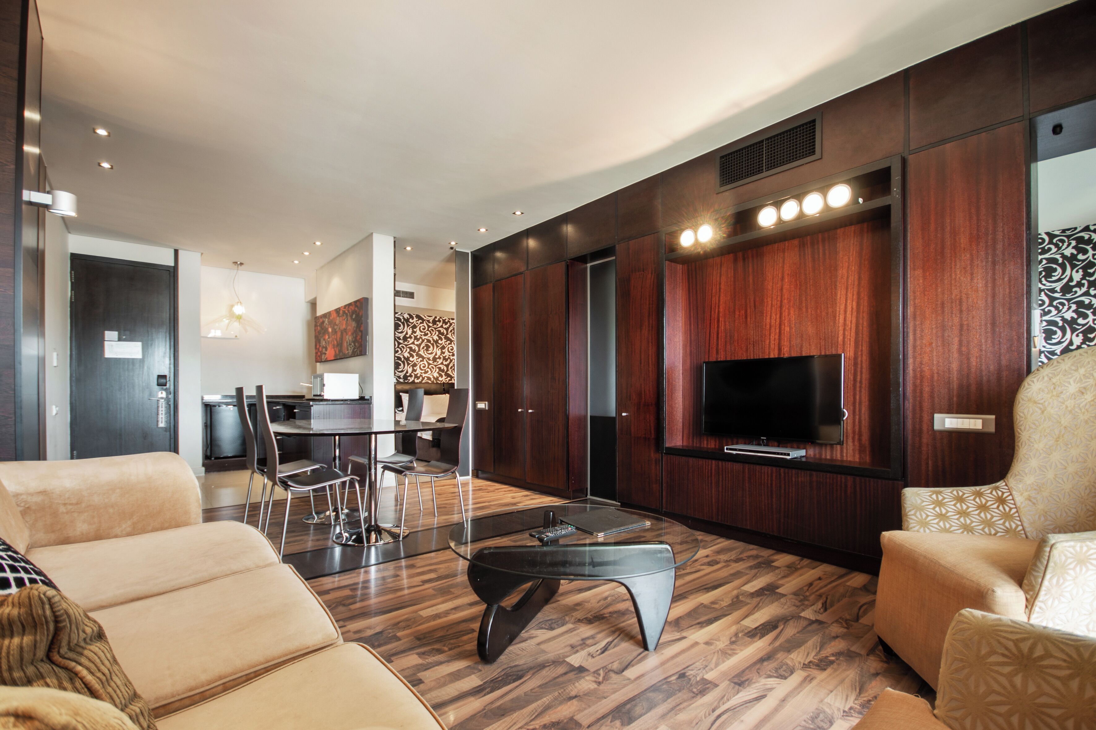 Een moderne woonkamer met een bank, een glazen salontafel, een televisie en een eethoek op de achtergrond.