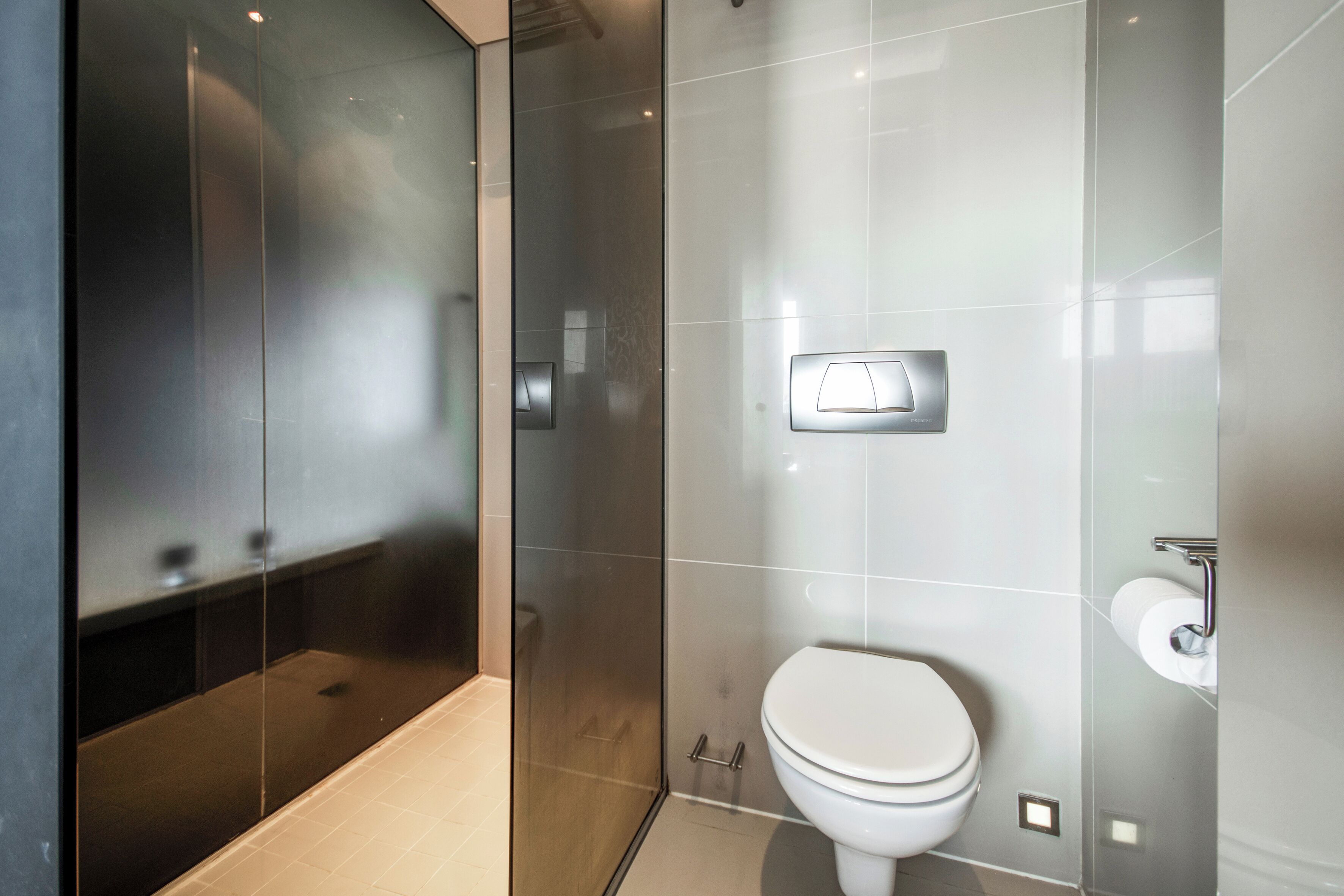 A modern bathroom with a glass shower enclosure, a toilet, and a wall-mounted light fixture.