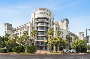 A hotel with a curved facade, multiple balconies, and palm trees in front.