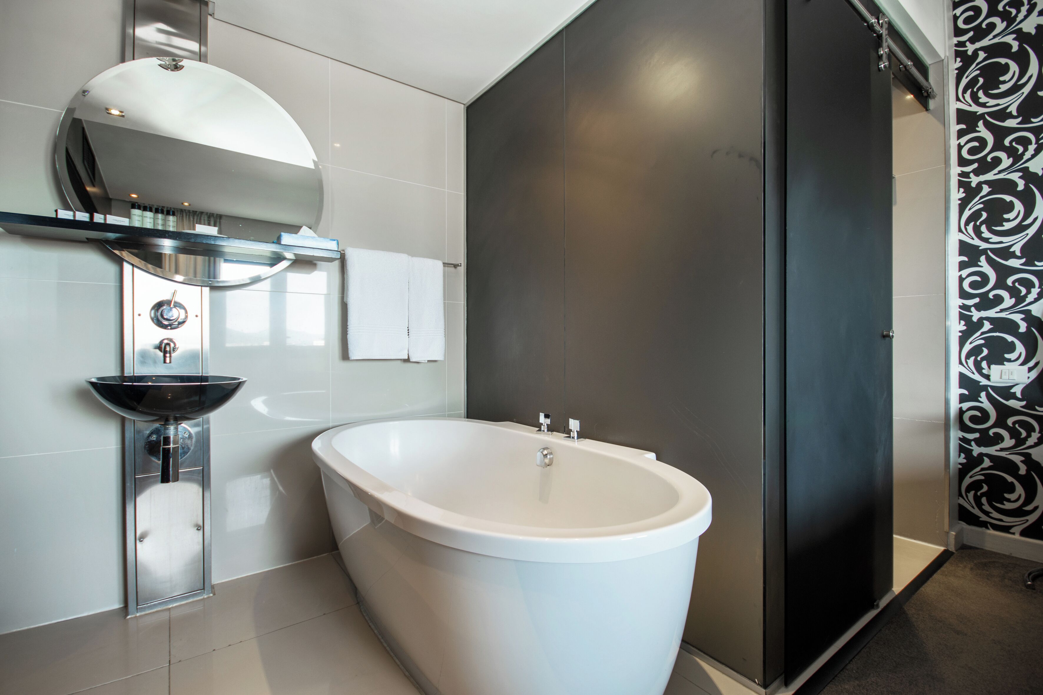 Un baño moderno con una bañera independiente, un lavabo de vidrio y un espejo grande sobre el lavabo.